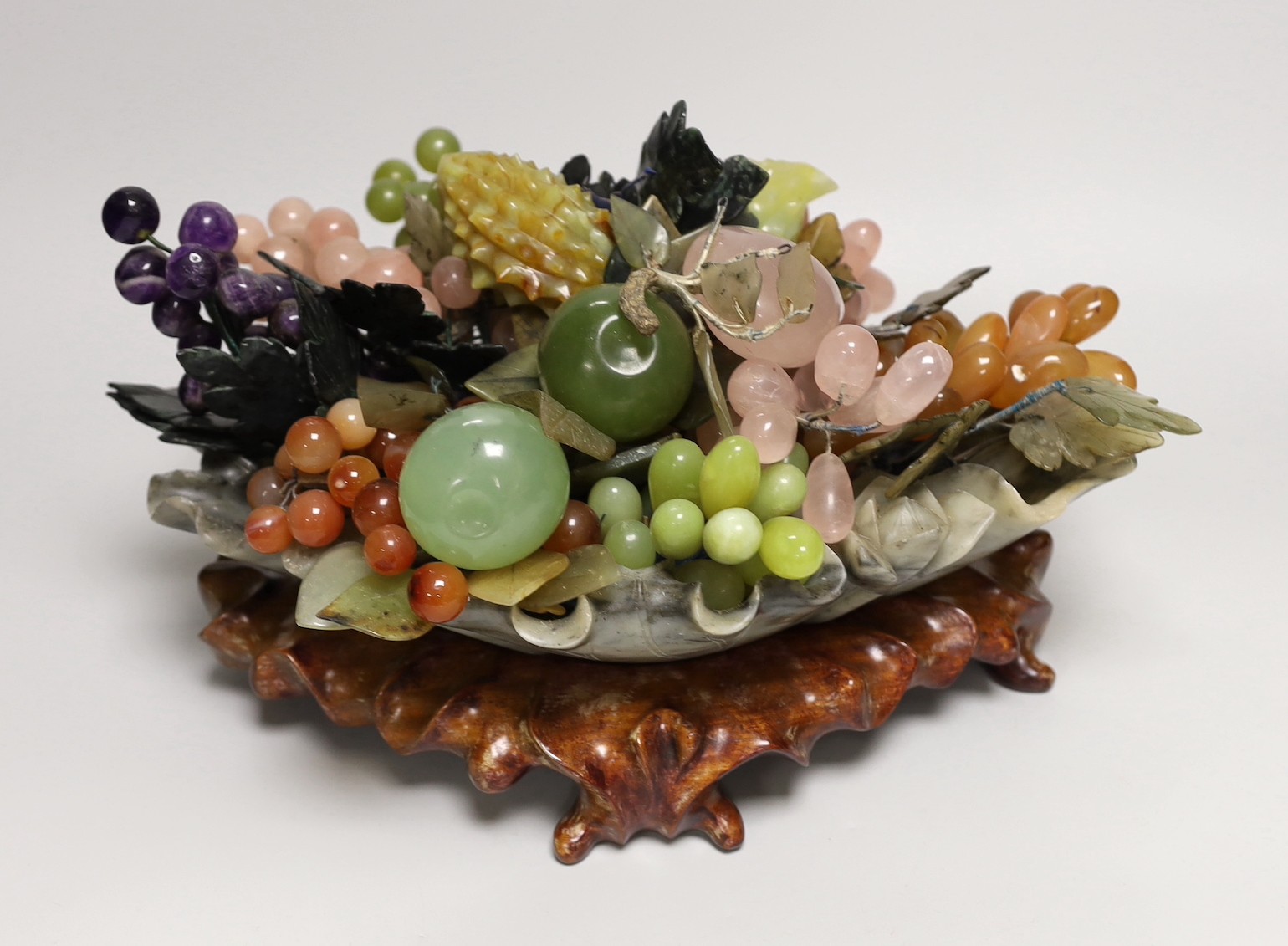 A Chinese soapstone dish of hardstone fruit on hardwood stand, 38cm wide